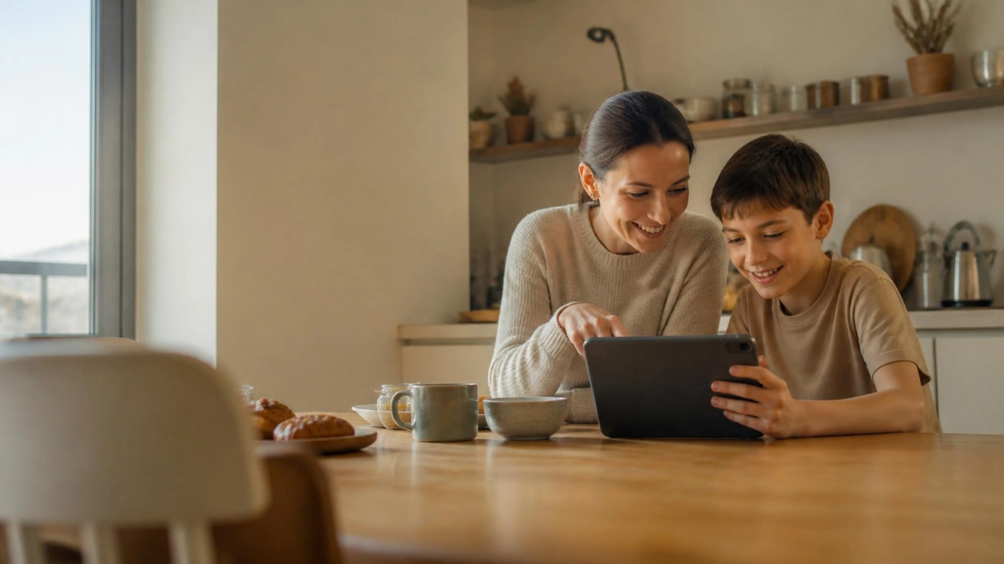 Eine Mutter und ihr Sohn schauen am Küchentisch gemeinsam auf ein Tablet