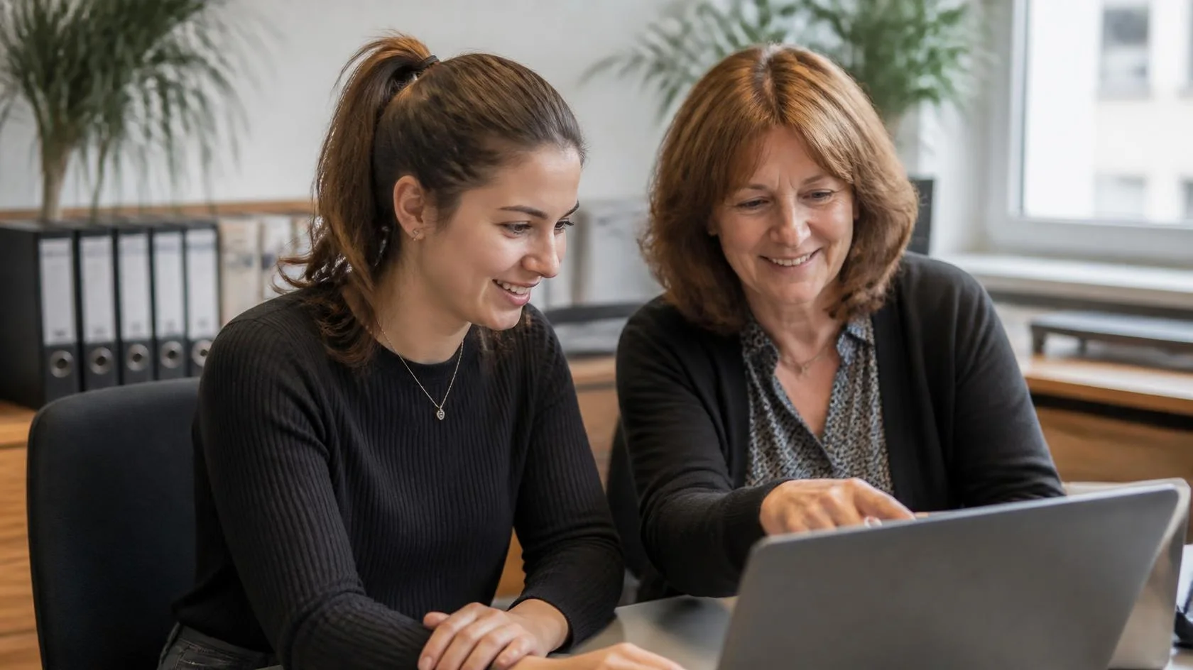 An experienced colleague and a trainee write an email on a laptop