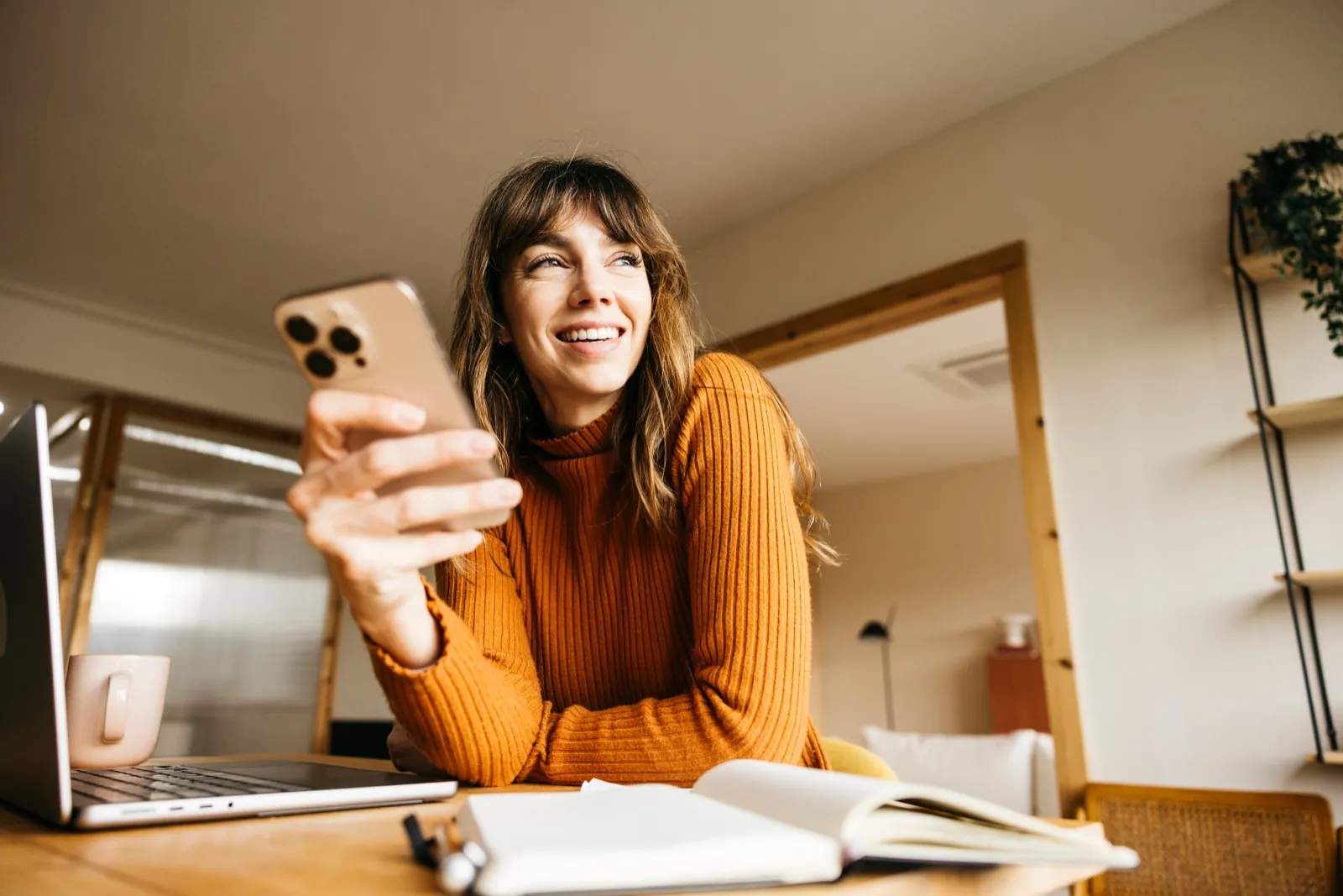 Eine Frau sitzt am Schreibtisch und schaut lächelnd auf ihr Handy